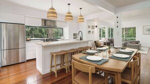 A modern kitchen with a central island, wooden chairs, and a dining table set for four. - Bangalow Retreat in Buderim (Mooloolaba Region)