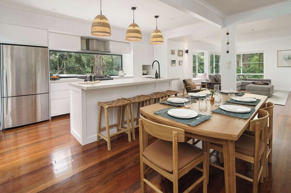 A modern kitchen with a central island, wooden chairs, and a dining table set for four. - Bangalow Retreat in Buderim (Mooloolaba Region)