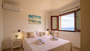 A bedroom with a bed, a nightstand, a window with a view of the sea, and an air conditioning unit. - Domus Aura villa in Sardinia with sea view and pool (Tertenia)