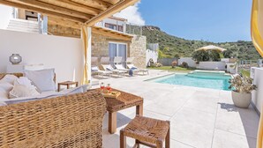 A modern outdoor living area with a pool, wicker furniture, and a stone building with a balcony. - Domus Aura villa in Sardinia with sea view and pool (Tertenia)