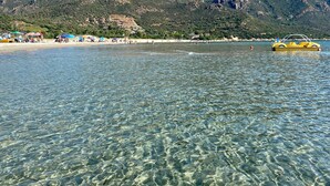 A clear lake with a mountain in the background and a beach with umbrellas.