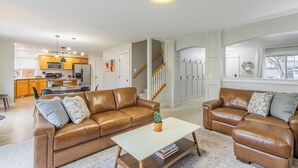 A spacious living room with a brown leather sofa set, a white coffee table, and a kitchen in the background. - Maple Suite Retreat: Arcade • Ping Pong • HomeGym • Toys • Pool • Playgrounds  (Meridian)