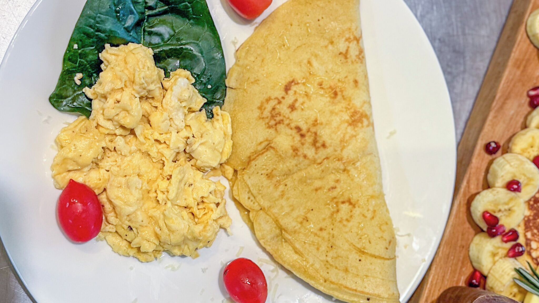 A plate with scrambled eggs, a spinach leaf, and a folded tortilla.