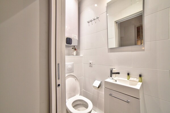 A modern bathroom with a toilet, sink, and mirror. - Cosy Studio - 2P - Strasbourg-saint-denis (Paris)