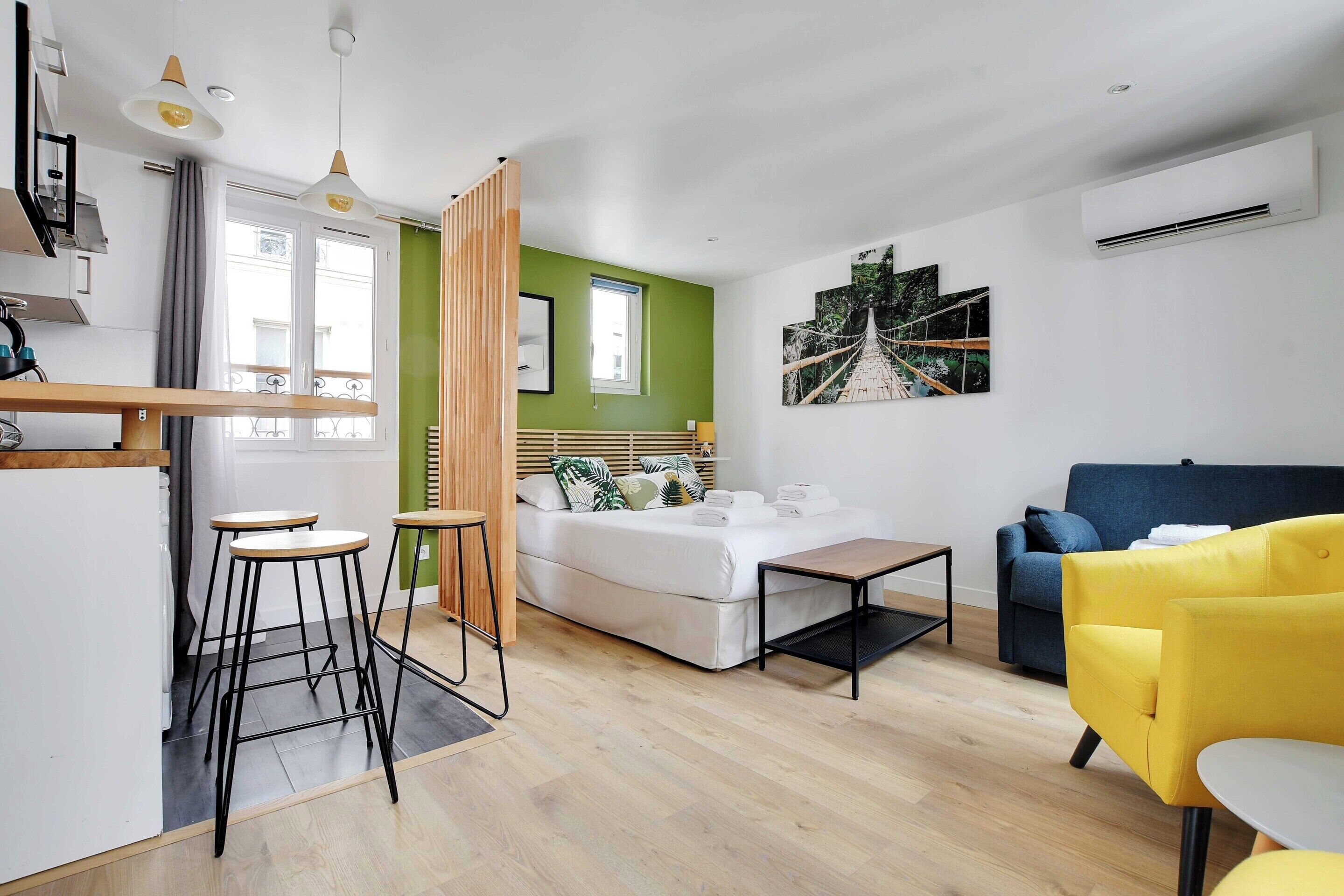 Un salon moderne comprenant un canapé, un coin repas avec des tabourets, un lit et un coin cuisine.