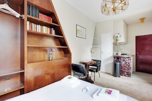 A hotel room with a wooden bookshelf, a desk with a chair, a bed with towels, and a marble counter. - Authentic Studio - 2P - Le Marais (Paris)