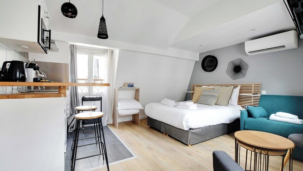 Une chambre d’hôtel moderne comprenant un lit, un canapé, une petite table à manger, un coin cuisine et un balcon.