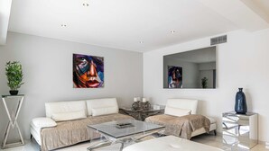 A modern living room with a sofa, a coffee table, and a side table. There are two paintings on the wall and a mirror above the sofa. - Beautiful 2P Apartment With Sunny Terrace (Cannes)