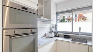 A modern kitchen with stainless steel appliances, a window with a view of buildings, and a sink with a faucet. - Beautiful 2P Apartment With Sunny Terrace (Cannes)