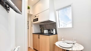 A compact kitchen with wooden cabinets, a microwave, a coffee maker, and a dining table with a white plate and wine glasses. - Cosy Studio - 2P - Strasbourg Saint-denis (Paris)