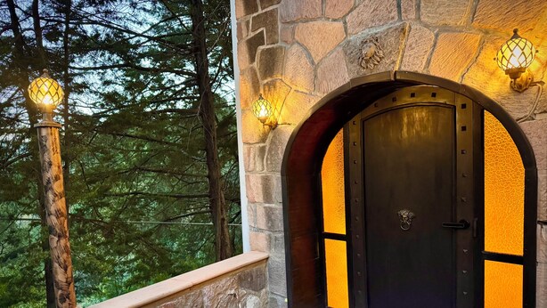 Ein Steinhaus mit dunklem, rundbogigen Eingang, einer Steinsäule und zwei Wandleuchten.