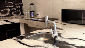 Eine Küche mit Marmorarbeitsplatte, einer Edelstahlspüle, einem modernen Wasserhahn, einem Mixer und einer schwarzen Mikrowelle.