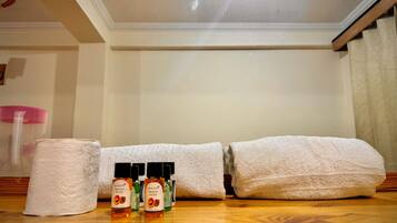 A bathroom with a wooden floor, a white towel, a roll of toilet paper, and two bottles of La Fleur Apricot body wash.