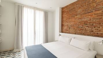 A hotel room with a large bed, a brick accent wall, a window with curtains, and a patterned floor.