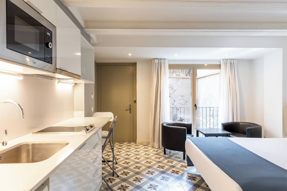 Une chambre d’hôtel équipée d’une kitchenette, d’un lit, d’un coin repas et d’un balcon avec des rideaux.