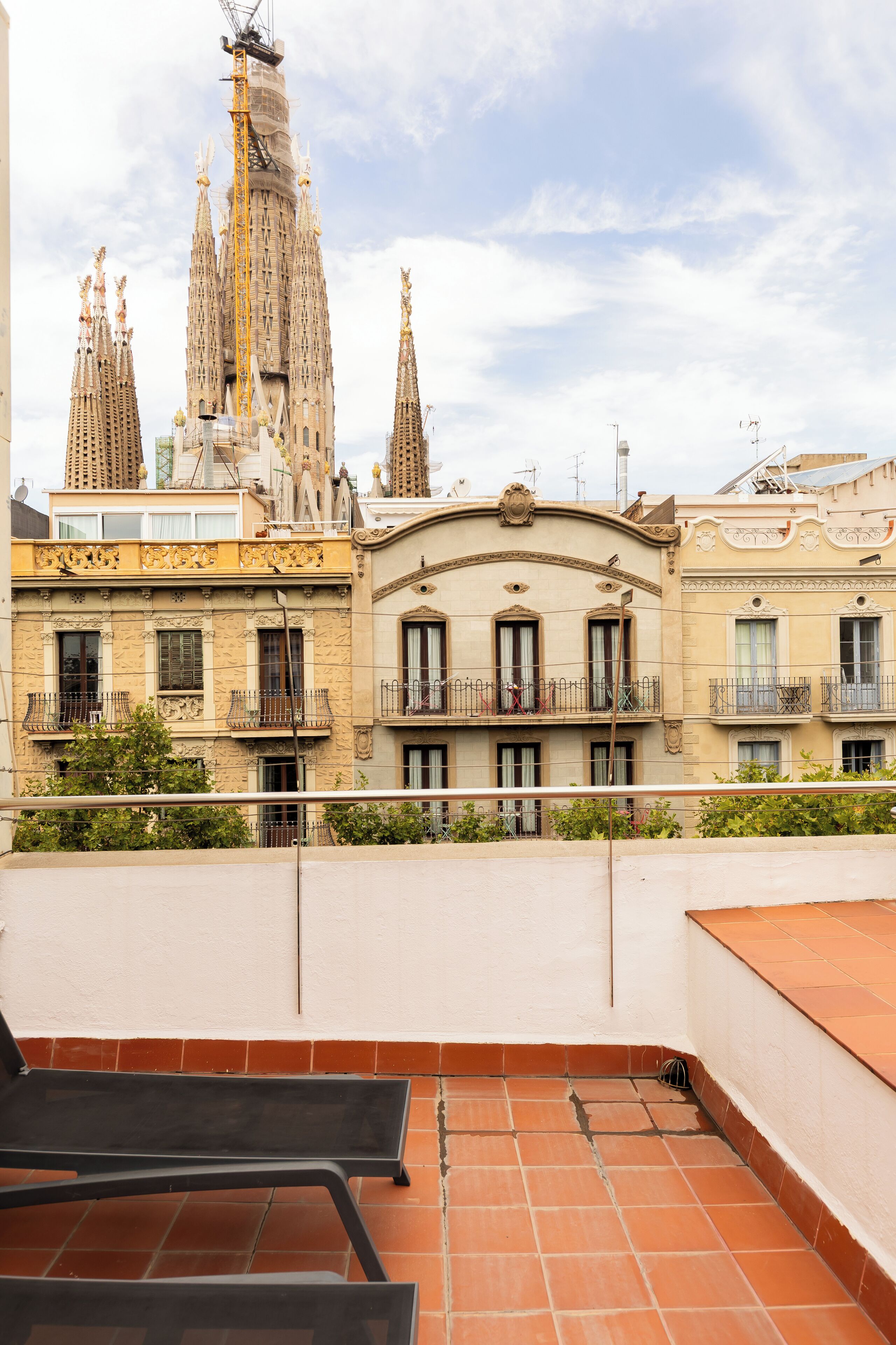 En takterrass med terrakottafärgade plattor, utsikt över Sagrada Familia och en byggnad med balkonger.