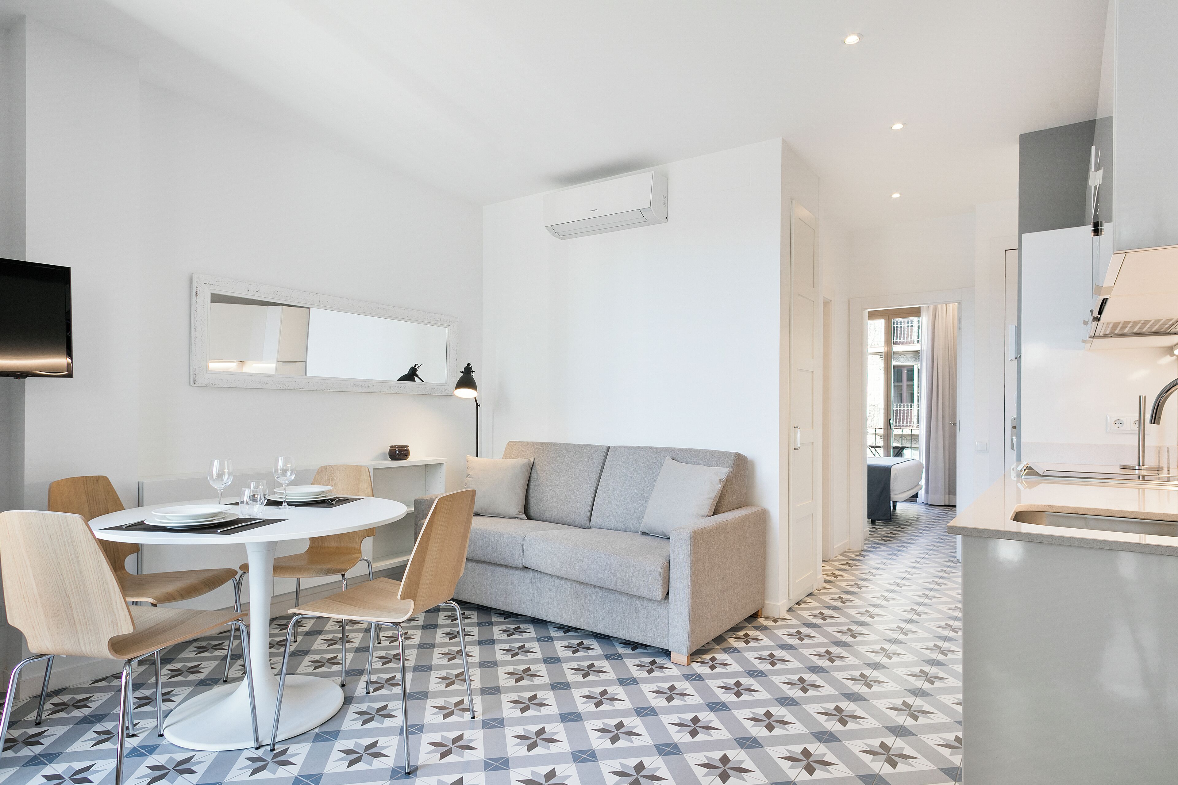 Un salon moderne avec une table à manger ronde, un canapé gris et des carreaux de sol à motifs.