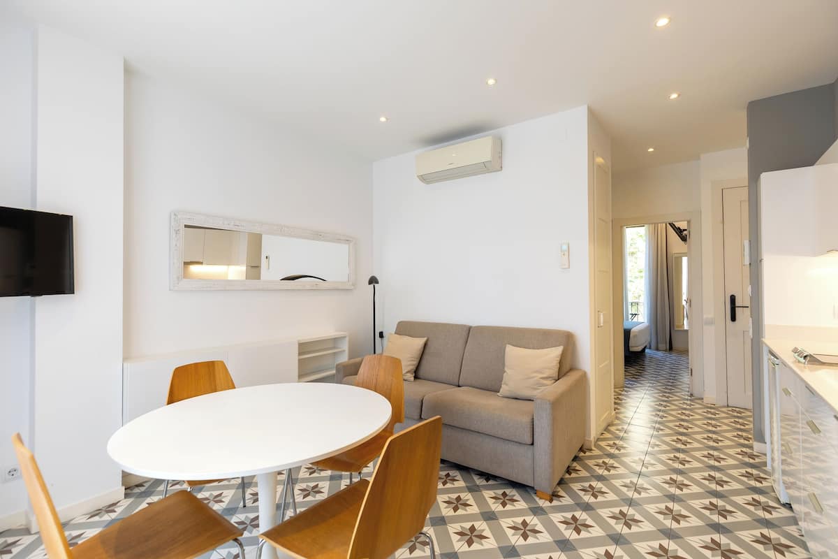 Un salon moderne avec une table ronde blanche, des chaises en bois, un canapé beige et un sol à motifs.