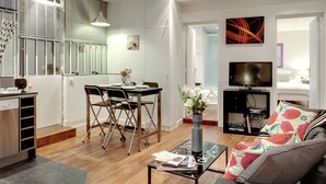 Ein modernes Wohnzimmer mit Essbereich, einem Fernseher und einer durch eine offene Tür einsehbarer Küche.