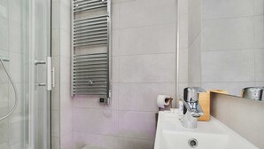 Moderni kylpyhuone, jossa on lasinen suihkuseinä, seinään kiinnitetty pyyhekoukku, peilillä varustettu pesuallas ja wc-istuin.