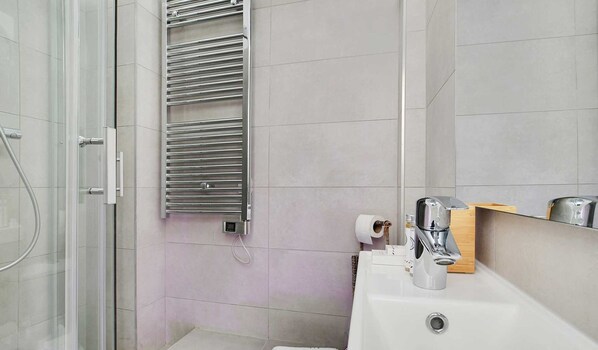A modern bathroom with a glass shower enclosure, a built-in towel rack, a sink with a mirror, and a toilet.