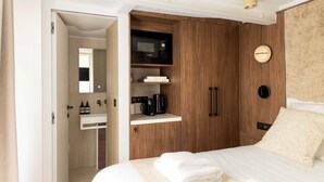 Een moderne hotelkamer met een houten garderobe, een magnetron, een koffiezetapparaat en een wekkerklok op het nachtkastje.