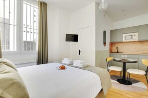 A hotel room with a bed, a small dining table with chairs, a microwave, and a TV mounted on the wall. - Comfortable Studio - 2P - Clignancourt/sacre-coeur (Paris)