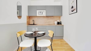 A compact kitchen with grey cabinets, a microwave, and a coffee maker. There is a dining table with two chairs and two wine glasses. - Comfortable Studio - 2P - Clignancourt/sacre-coeur (Paris)