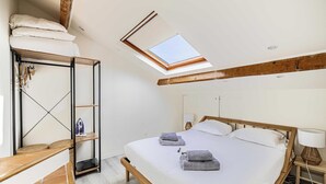 Una camera da letto con un lucernario, un letto con cuscini e asciugamani, una panca in legno e uno scaffale con una lampada.