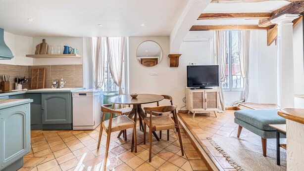 Una cucina compatta con zona pranzo, televisione e finestra con tende.