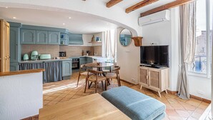 Una cucina moderna con mobili azzurri, un'area pranzo con un tavolo rotondo e sedie, una televisione e un'ampia finestra con tende.