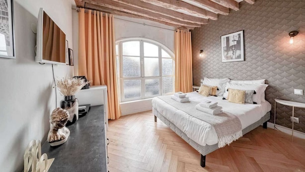 A bedroom with a large bed, a window with curtains, a wall-mounted TV, and a small bedside table. - Apartment in Paris for 2 People (Paris)