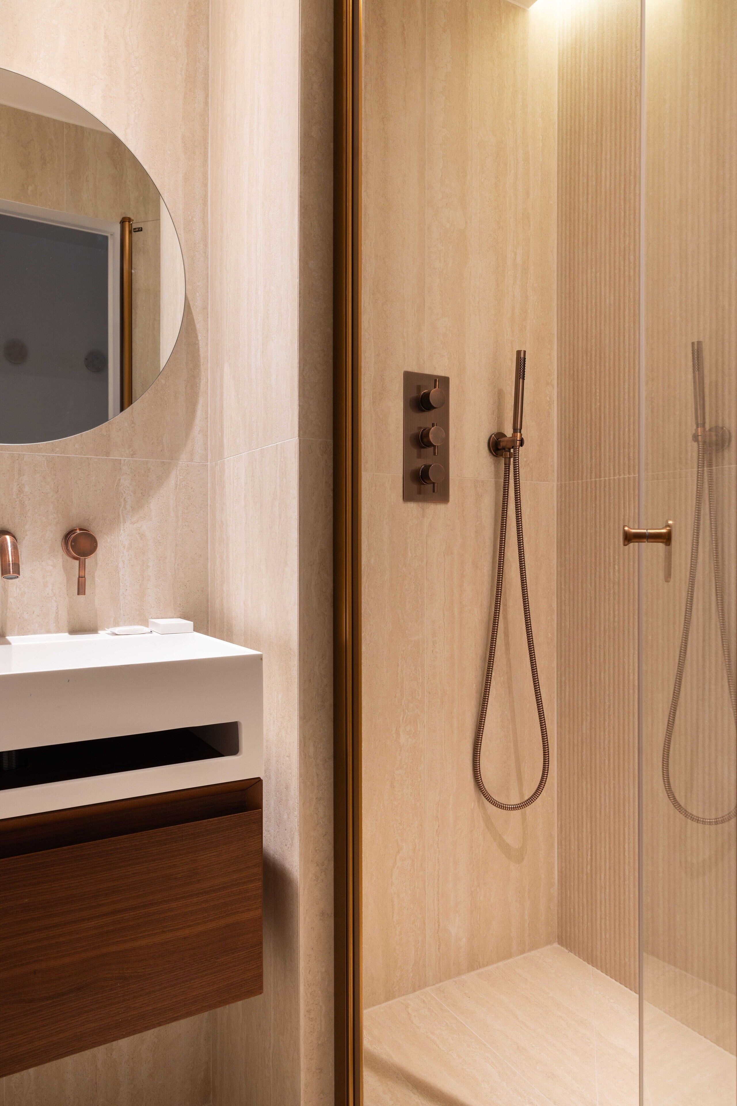 Une salle de bain moderne avec un lavabo blanc, un miroir rond et une douche séparée par des parois en verre.