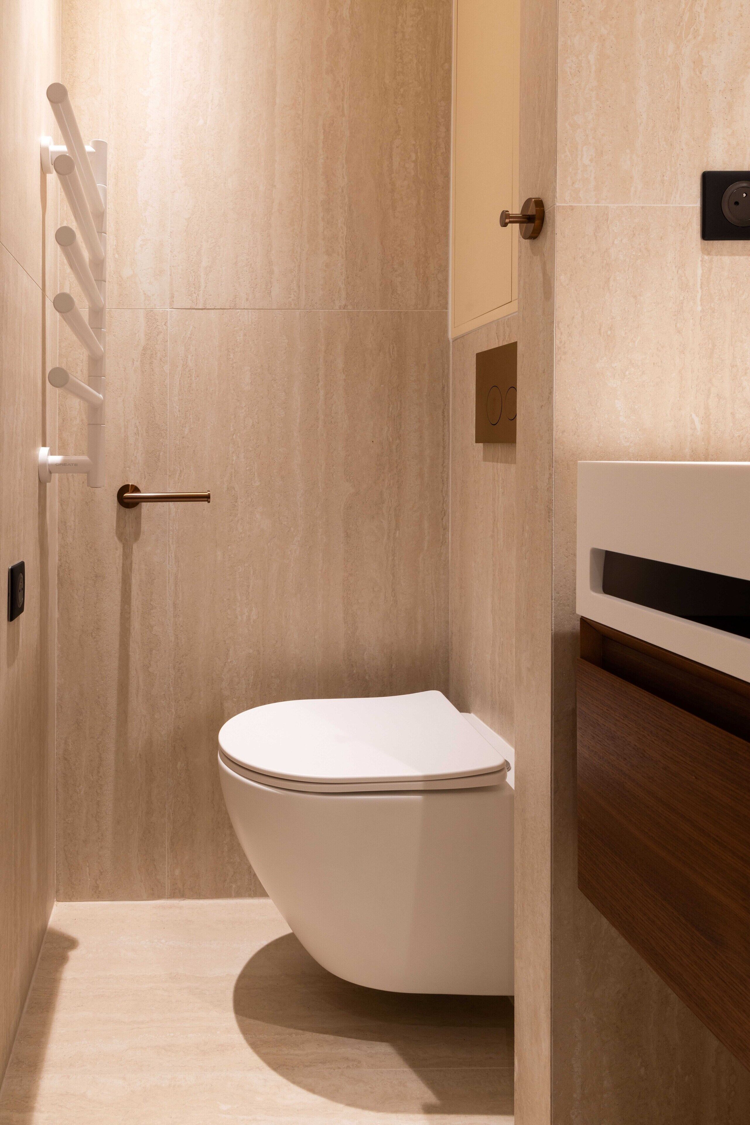 A modern bathroom with a toilet, a towel rack, and a wooden vanity.