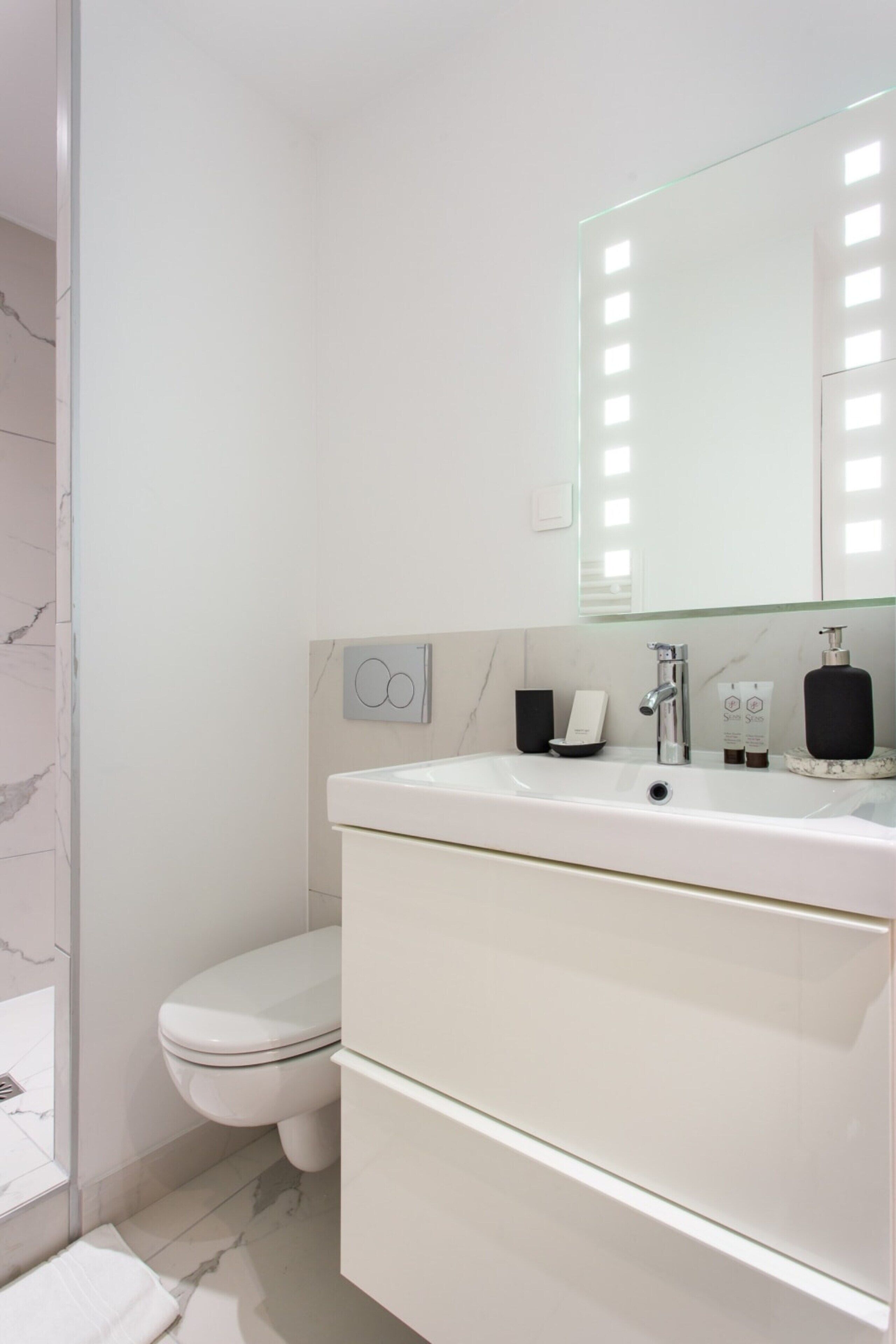 A modern bathroom with a white sink, mirror, and toilet.