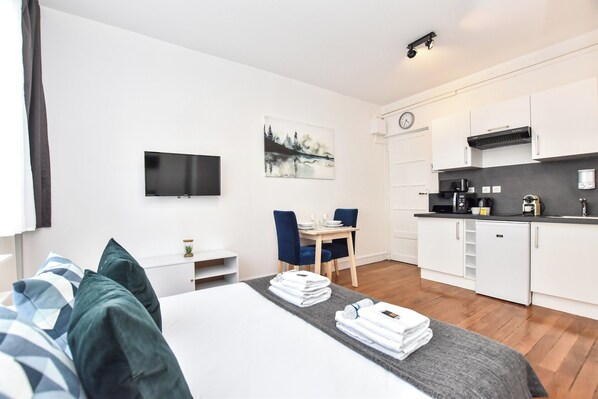 A modern hotel room with a bed, a desk, a chair, a TV, a painting, and a kitchenette. - Cosy Studio - 2P - Bastille (Paris)