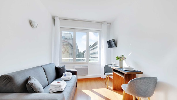 A modern living room with a grey sofa, a wooden coffee table, and a TV mounted on the wall. - Charming Studio - 2P - Parc Georges Brassens (Paris)