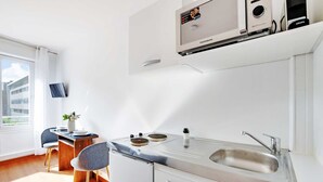 A modern kitchen with a built-in microwave, a sink, and a dining area with a table and chairs. - Charming Studio - 2P - Parc Georges Brassens (Paris)