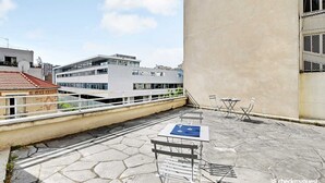 A rooftop terrace with a table and chairs, a satellite dish, and a view of surrounding buildings. - Charming Studio - 2P - Parc Georges Brassens (Paris)