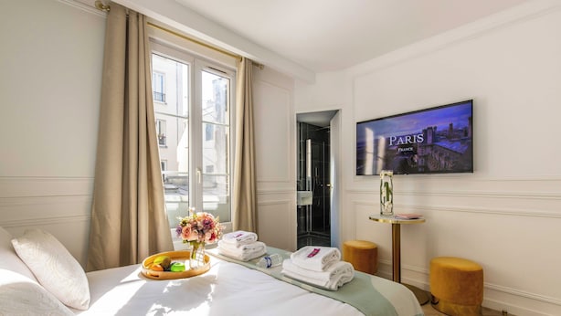 Ein Hotelzimmer mit Bett, einem fenster mit Vorhängen, einem Gemälde von Paris und einem Tisch mit Handtüchern und einer Obstschale.