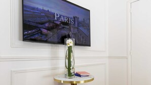 Ein Zimmer mit einem runden Tisch, zwei goldfarbenen Poufs, einem gerahmten Bild von Paris und einer weißen Tür.