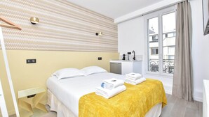 A hotel room with a bed, a yellow throw blanket, towels, a small table, a wall-mounted light, and a window with a view of buildings. - Quiet Studio - 2P - Javel / Eiffel Tower (Paris)