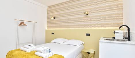 A hotel room with a bed, a bedside table with a sink, a towel rack, and a patterned wall.