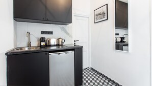 A compact kitchen with a black countertop, stainless steel appliances, and a checkered floor. - Charming Studio - 4P - Place de la Bastille (Paris)