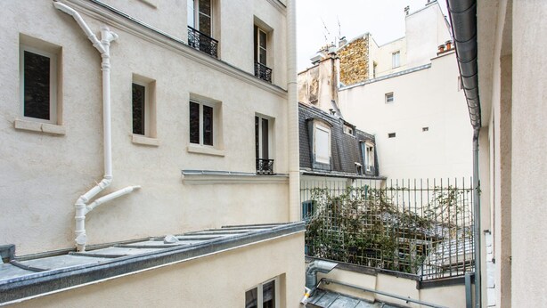 A narrow urban alleyway with buildings on either side, featuring balconies, windows, and a small garden area with a metal fence. - Charming Studio - 4P - Place de la Bastille (Paris)
