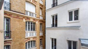 A narrow alleyway between two multi-story buildings with brick and plaster facades, featuring multiple windows and balconies. - Charming Studio - 4P - Place de la Bastille (Paris)