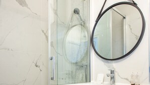 A bathroom with a glass shower enclosure, a wooden vanity with a mirror, and marble walls. - Charming Studio - 4P - Place de la Bastille (Paris)