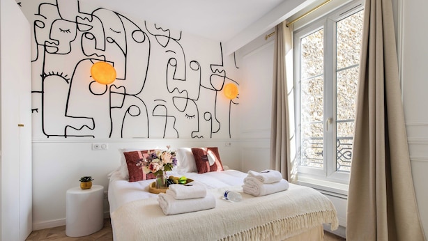 Ein modernes Schlafzimmer mit einem großen Bett, einem Wandbild und einem Fenster mit Vorhängen.