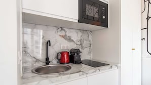 Eine Küche mit Marmorarbeitsplatte, einem Spülbecken, einem roten Wasserkocher und einer schwarzen Kaffeemaschine.