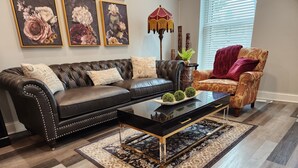Un salon avec un canapé en cuir noir, un fauteuil à motifs, une table basse noire et une lampe décorative.